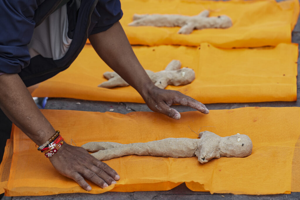 Man shaping dough on orange surface with several dough pieces in the background.
