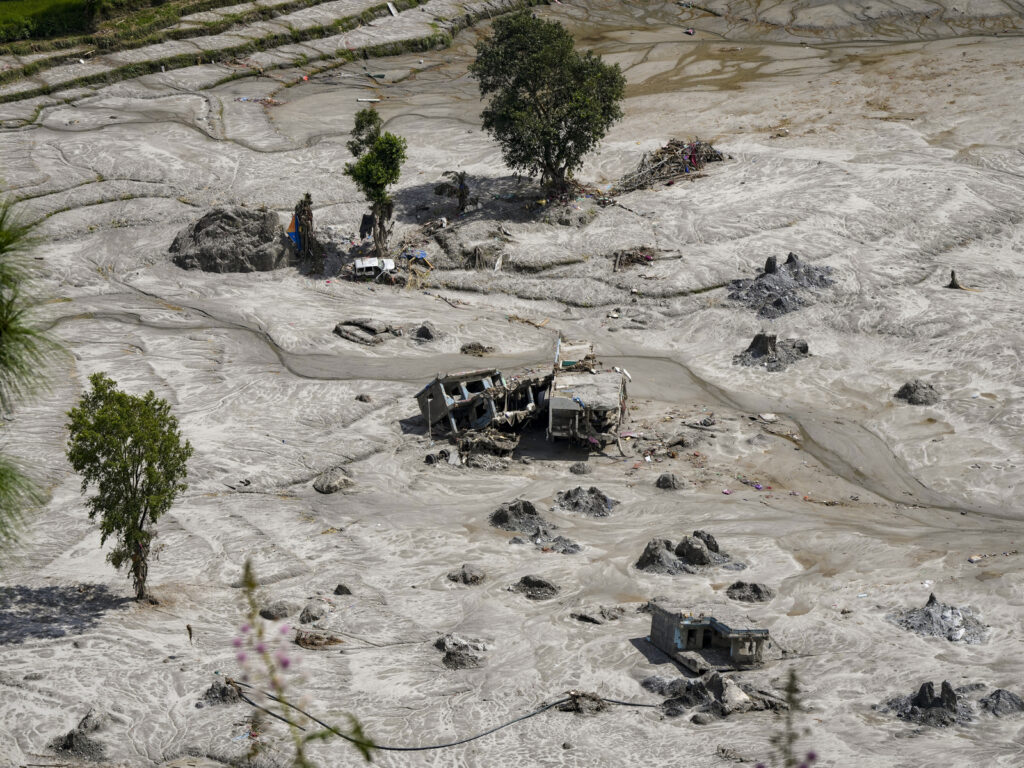 Flooded landscape with damaged vehicles and scattered debris after a natural disaster.