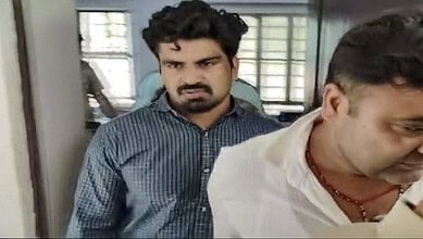 Man in white shirt and man in blue shirt in a room with windows and metal bars.