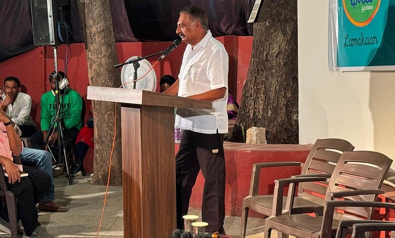 Man speaking at a podium during an outdoor event with audience members watching.