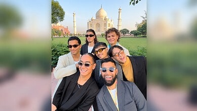 Group of diverse friends smiling in front of the Taj Mahal during daytime.