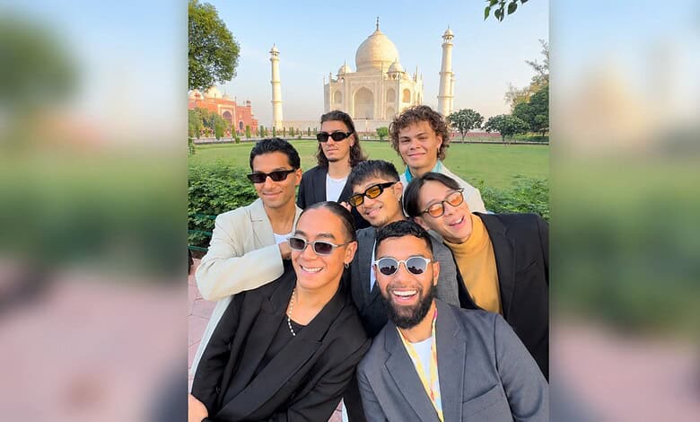 Group of diverse friends smiling in front of the Taj Mahal during daytime.