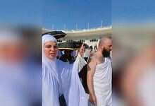 Rakhi praying with others near a cruise ship in Mecca under a clear blue sky.