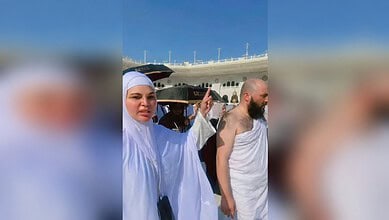 Rakhi praying with others near a cruise ship in Mecca under a clear blue sky.