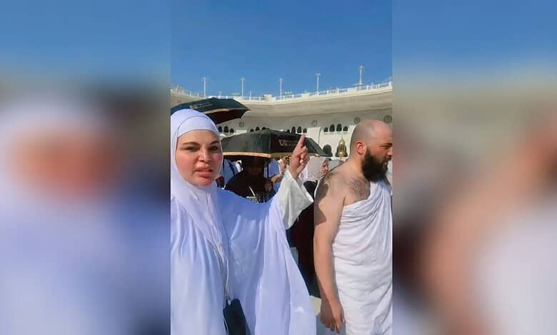 Rakhi praying with others near a cruise ship in Mecca under a clear blue sky.