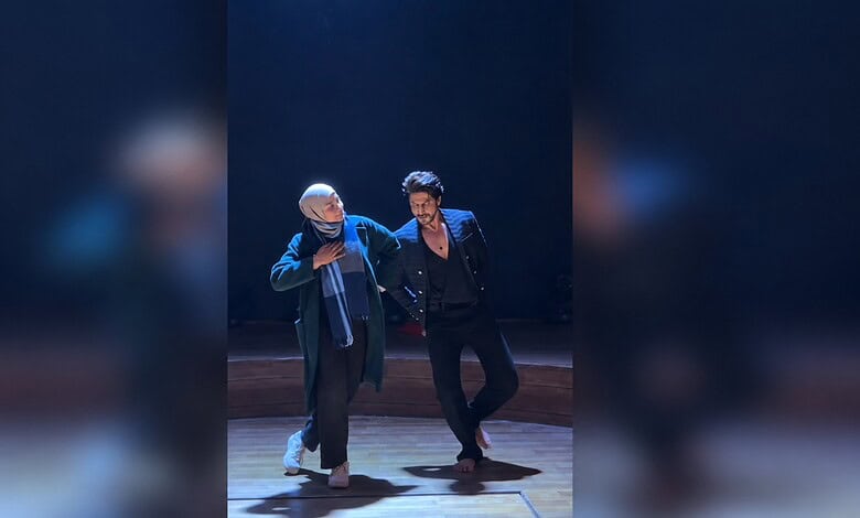 Shah Rukh Khan dancing with a fan on stage during a live event.