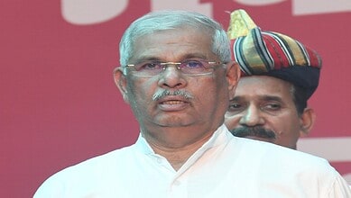 Keralam Guv speaking at a public event with a man in traditional attire in the background.