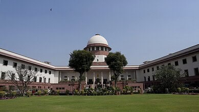 Supreme Court of India building with lush green lawn and clear blue sky.