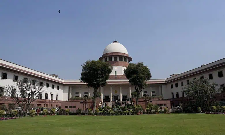Supreme Court of India building with lush green lawn and clear blue sky.