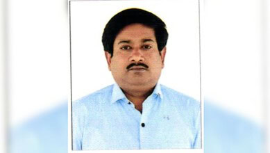 Portrait of a man with black hair and moustache wearing a light blue shirt.