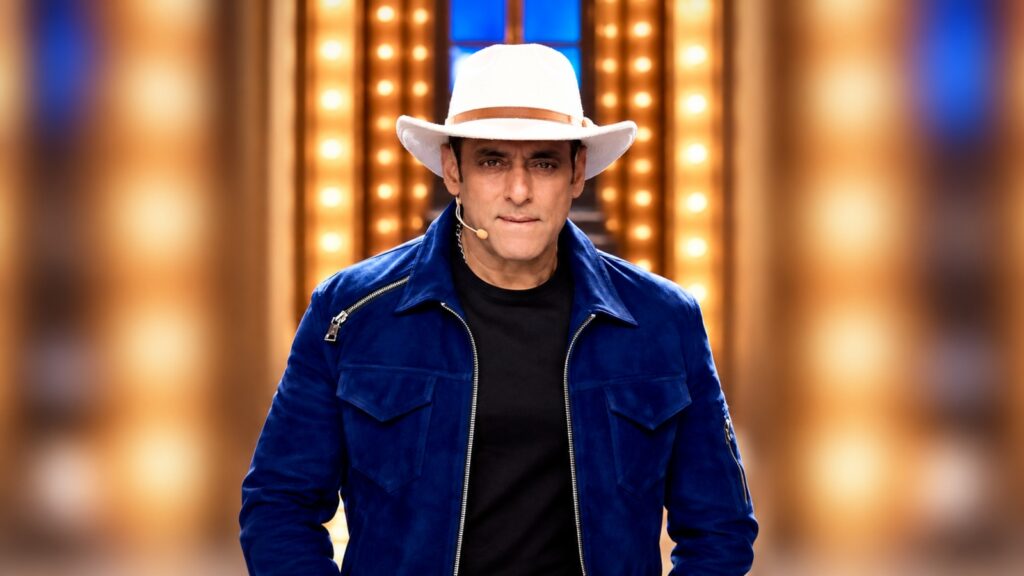 Salman Khan in a blue jacket and white hat on a brightly lit stage.