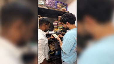 Two men browsing books in a bookstore, one holding a book and the other pointing at it.