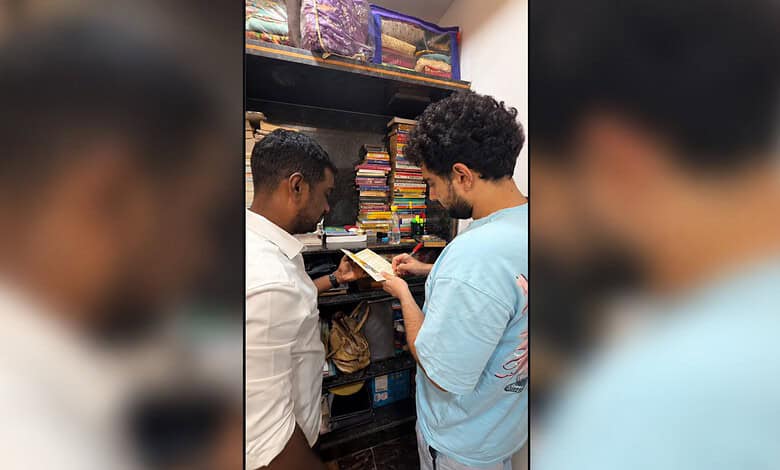 Two men browsing books in a bookstore, one holding a book and the other pointing at it.