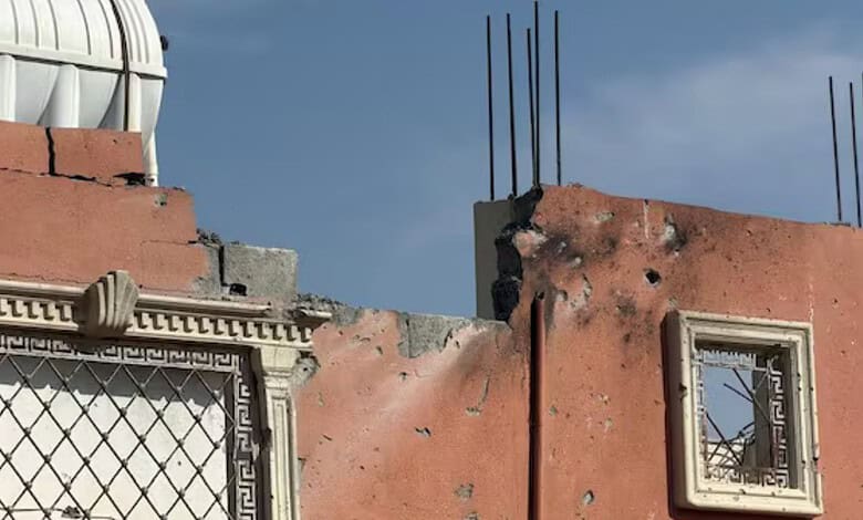 Damaged building with exposed rebar and broken wall sections under a cloudy sky.