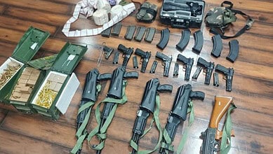 Arms and ammunition seized, including guns, magazines, and tactical gear, displayed on a wooden surface.