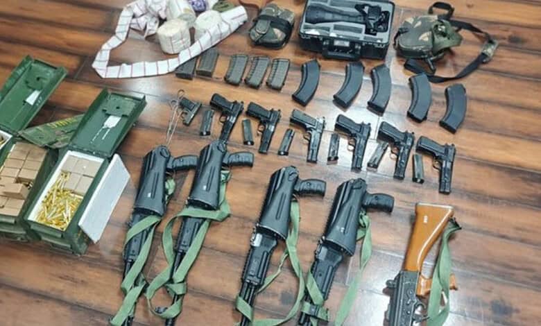 Arms and ammunition seized, including guns, magazines, and tactical gear, displayed on a wooden surface.