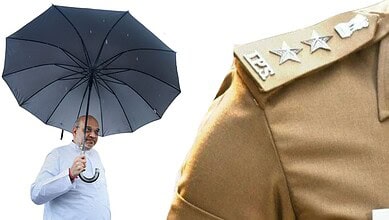 Indian man holding a black umbrella, wearing a white shirt, with a police uniform shoulder visible.