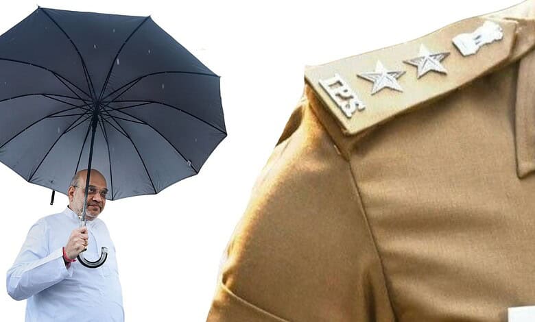 Indian man holding a black umbrella, wearing a white shirt, with a police uniform shoulder visible.