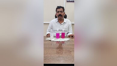 Man sitting at a table with three pink bottles and a white cloth, in an indoor setting.
