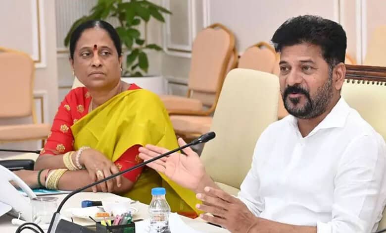 Konda Surekha speaking during a meeting with a woman in a yellow saree in the background.
