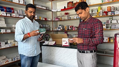 Two men inspecting medicines in a pharmacy, shelves filled with drugs in the background.