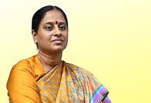 Indian woman in traditional saree with a serious expression against a yellow background.