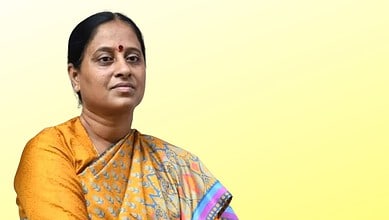 Indian woman in traditional saree with a serious expression against a yellow background.