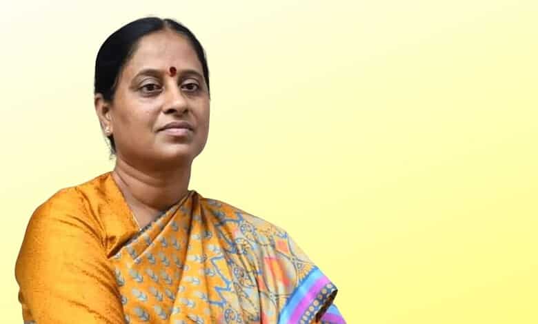 Indian woman in traditional saree with a serious expression against a yellow background.