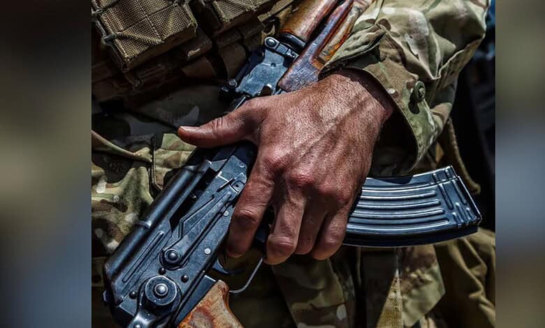 Close-up of a soldier's hand holding a rifle in camouflage uniform.