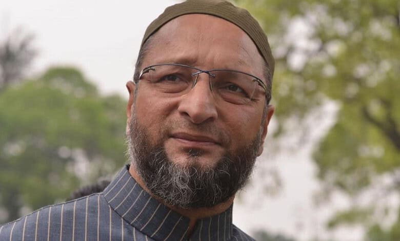 Owaisi speaking outdoors with trees in the background, wearing glasses and a cap.