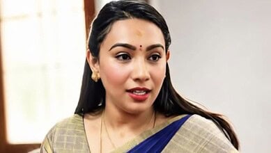 Young woman with traditional Indian attire and jewelry, smiling indoors.