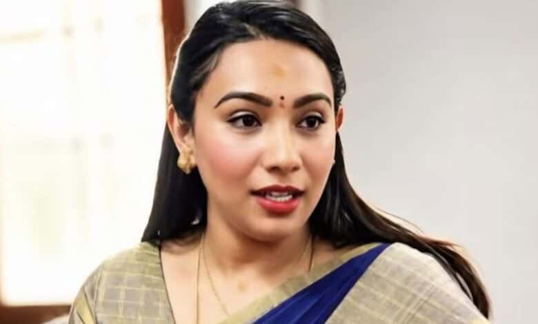 Young woman with traditional Indian attire and jewelry, smiling indoors.
