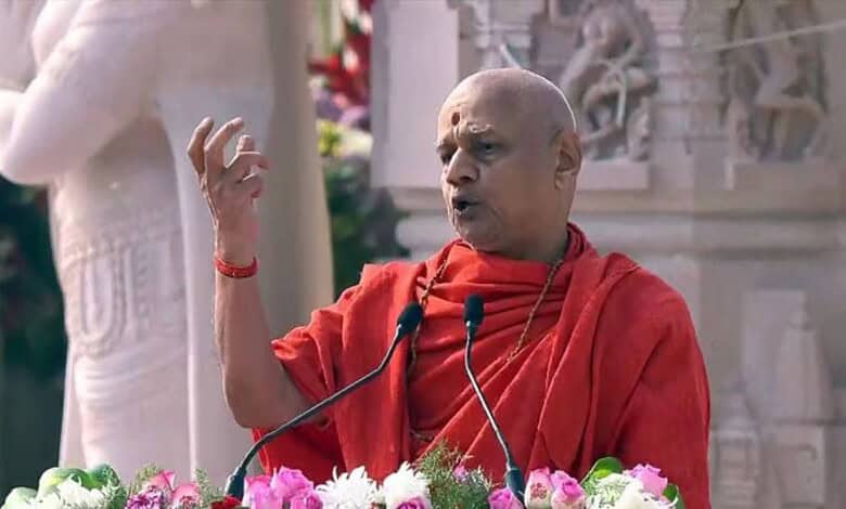 Govind Dev Giri speaking at a religious event with a temple backdrop.