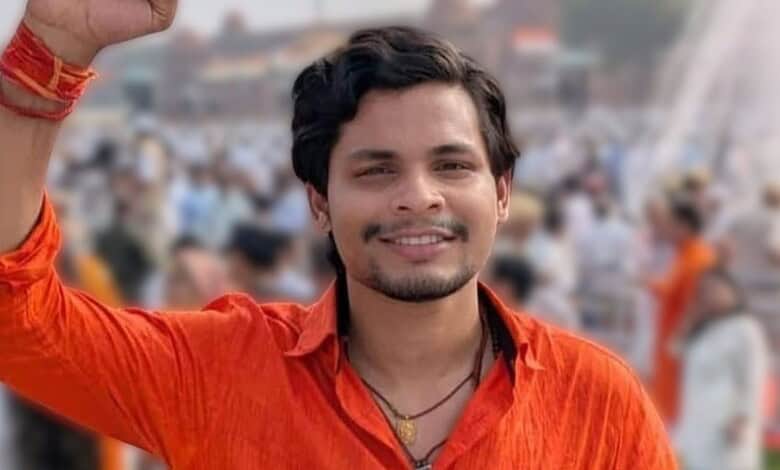 Young man smiling and raising his hand at a crowded outdoor event in India.