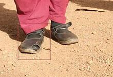 Child's worn-out school shoes on dusty ground, showing poor quality and quick wear.