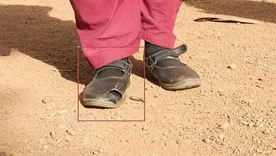 Child's worn-out school shoes on dusty ground, showing poor quality and quick wear.