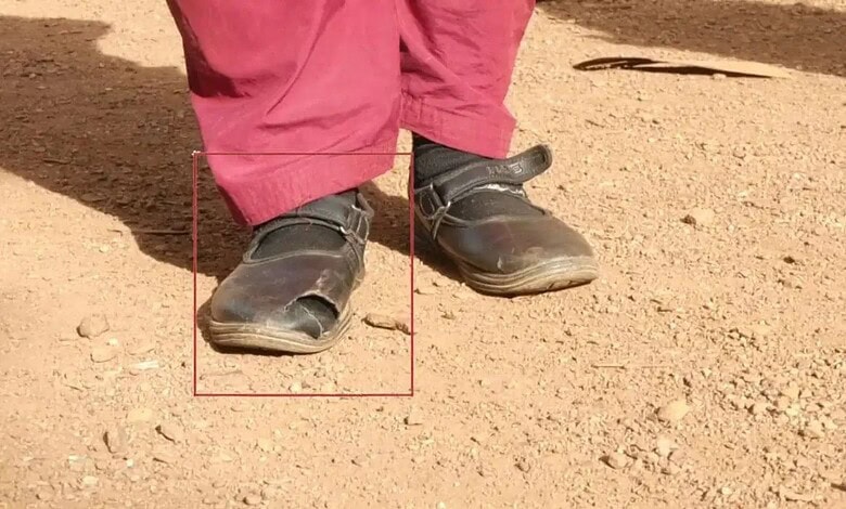 Child's worn-out school shoes on dusty ground, showing poor quality and quick wear.