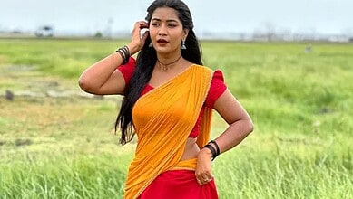 Young woman in traditional yellow and red saree standing in green field, looking concerned.