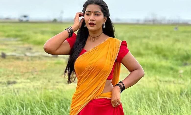 Young woman in traditional yellow and red saree standing in green field, looking concerned.