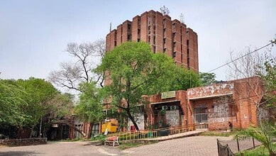 JNU campus building with trees and a pathway, under a cloudy sky.