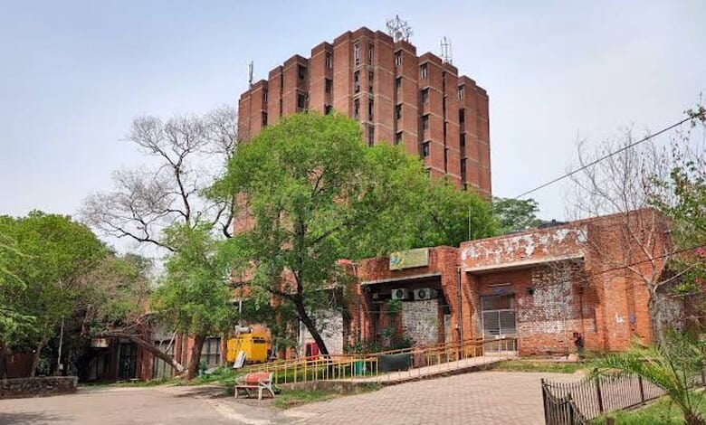 JNU campus building with trees and a pathway, under a cloudy sky.