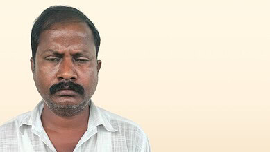 Man with a serious expression, dark hair, and a white shirt against a plain background.