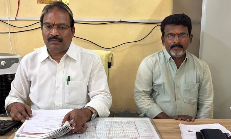 Two men sitting at a desk with documents, in an office setting.