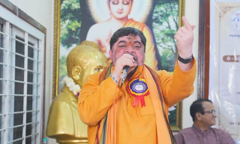 Ponnam Srinivas speaking at a political event with a large portrait of Buddha in the background.