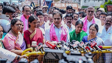 Political leader addressing media with supporters and microphones at a press conference.