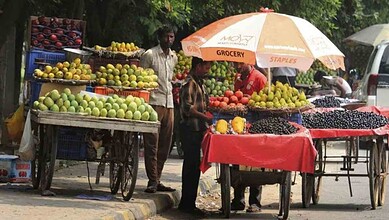 Street vendors selling fruits at a busy market in Delhi under umbrellas.