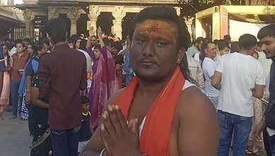 Man with orange scarf and religious markings in a crowded outdoor setting.