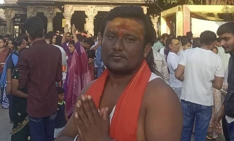 Man with orange scarf and religious markings in a crowded outdoor setting.