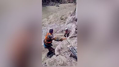 Rescue workers assist in flood-affected area with muddy terrain and debris.