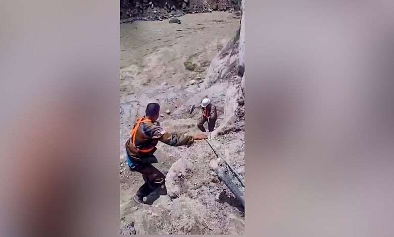 Rescue workers assist in flood-affected area with muddy terrain and debris.